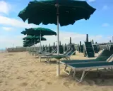 Filettato lido verde San Cataldo, con file di lettini e ombrelloni verdi sotto un cielo azzurro con nuvole bianche.