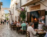Cosa vedere a Cisternino in mezza giornata: vicoli bianchi, fiori colorati e un macellaio che griglia carne all'aperto.