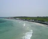 Vista aerea del lido Le Cesine, con acque turchesi e una spiaggia affollata di bagnanti e ombrelloni rossi.