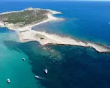 L'isola delle Correnti, leggenda di sabbia e mare cristallino, con un faro bianco e barche che solcano le acque turchesi.