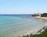 Acque cristalline e scogliere rocciose sulla spiaggia delle Formiche, Portopalo di Capo Passero. Un faro solitario veglia sul mare.
