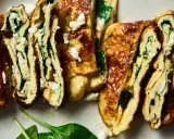 Rotoli di pisci d'ovu con spinaci e formaggio feta, dorati e invitanti, tagliati a fette per mostrare il ripieno cremoso.