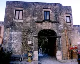 Ingresso di un baglio, con arco in pietra e muri antichi. Un piccolo chiosco vende souvenir.