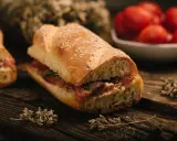 Panino con pomodoro e acciughe, un classico della cucina povera siciliana, su tagliere in legno con erbe aromatiche.