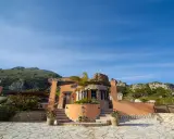 Il castello di Baida, con la sua architettura unica, si erge su un terreno roccioso sotto un cielo azzurro.