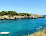 Acque cristalline e scogliere rocciose, un angolo di paradiso tra le spiagge Salento. Una piccola barca bianca galleggia tranquilla.