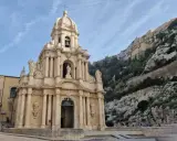 La chiesa barocca di San Giuseppe a Scicli, con il suo Cristo in gonnella, si erge maestosa contro una scogliera rocciosa.