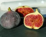 Un intero fico viola e due metà succose rivelano la dolcezza di una varietà di fichi siciliani, con la loro polpa rossa e i semi dorati.