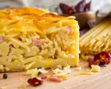 Fetta di spaghetti al forno, uno dei piatti tipici napoletani, con pancetta e formaggio. Sullo sfondo, spaghetti crudi e peperoncini.