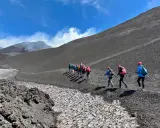 Escursionisti sul fianco di quello che i siciliani chiamano l'Etna, con fumo che sale dalla cima.