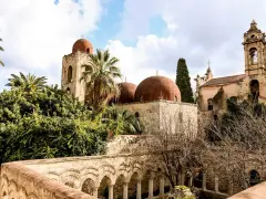 Le iconiche cupole rosse di Palermo si stagliano tra palme e vegetazione lussureggiante, un'antica bellezza sotto un cielo nuvoloso.