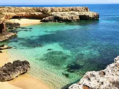 Una caletta nascosta con sabbia dorata e acque cristalline, tipica del mare in Puglia. Rocce calcaree scolpite dal vento incorniciano questo angolo di paradiso.