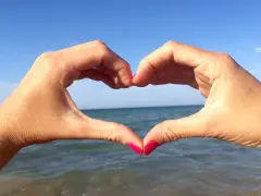 Mani a cuore con sfondo mare e cielo azzurro. Il suono del mare, u scrusciu du mari, evoca pace e amore.