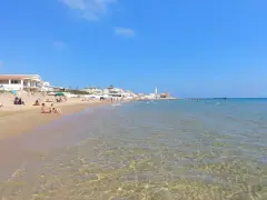 La spiaggia di Montalbano, con case bianche e gente che prende il sole e fa il bagno, sotto un cielo azzurro.