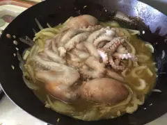 Polpi murati cotti in padella con cipolle e un sugo dorato. Le ventose dei tentacoli sono ben visibili.