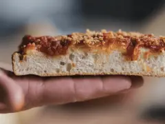 Una fetta di sfincionello palermitano, con la sua soffice mollica e il sugo rosso, tenuta in mano.