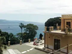 Vista mare dalla villa Bosurgi a Messina, con alberi tropicali e un veliero all'orizzonte.