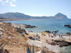 La **spiaggia di Isulidda** è affollata di bagnanti sotto ombrelloni colorati. Il mare azzurro invita a un bagno rinfrescante, mentre le montagne sullo sfondo creano un panorama mozzafiato.