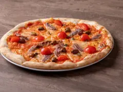 Pizza fuata siciliana con pomodorini, acciughe, olive e capperi su un piatto bianco, su un tavolo di legno.
