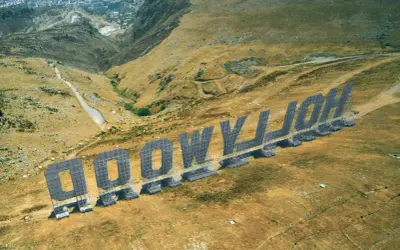 Aerial view of the "HOLLYWOOD" sign in Palermo, Italy, set against a dry, hilly landscape.