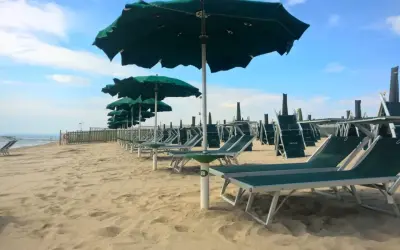 Filettato lido verde San Cataldo, con file di lettini e ombrelloni verdi sotto un cielo azzurro con nuvole bianche.