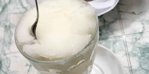 Un bicchiere colmo di granita al gelsomino, con un cucchiaino che affonda nella sua consistenza ghiacciata. Perfetta per una pausa rinfrescante.