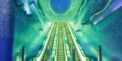 La fermata metro Napoli Toledo, famosa per la sua arte e design, con scale mobili che sembrano scendere verso un mare di mosaici blu e verdi.