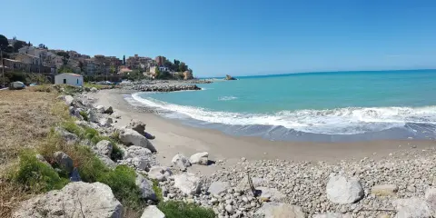 Spiaggia di Lampare a Tusa, con mare turchese, case colorate sul promontorio e rocce sulla riva.