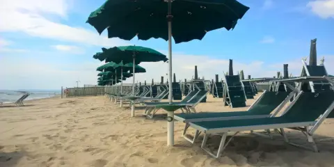 Filettato lido verde San Cataldo, con file di lettini e ombrelloni verdi sotto un cielo azzurro con nuvole bianche.