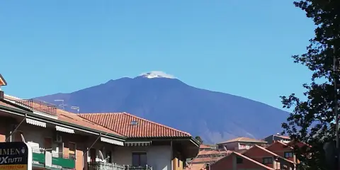 Vista dell'Etna fumante, un'imponente montagna che domina il paesaggio. Un'ottima meta per scoprire cosa vedere a Bronte, con i suoi tetti rossi in primo piano.