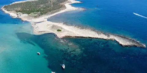 L'isola delle Correnti, leggenda di sabbia e mare cristallino, con un faro bianco e barche che solcano le acque turchesi.