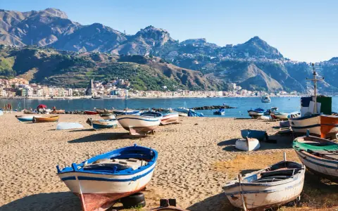 Barche da pesca sulla spiaggia di Giardini Naxos, con Taormina sullo sfondo montuoso.