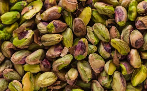 Un mucchio di pistacchi, alcuni con il guscio screpolato che rivela il loro interno verde brillante, ricordano il sapore del pistacchio in siciliano.