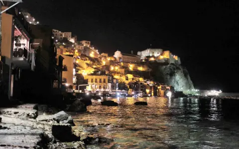 Scilla illuminata di notte, un incanto da visitare a piedi. Case colorate e il castello arroccato sul promontorio si specchiano nel mare.