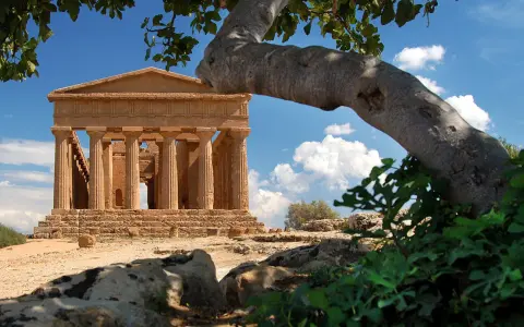 Tempio greco dorico, parte del patrimonio UNESCO Sicilia, si staglia sotto un cielo azzurro con nuvole bianche.