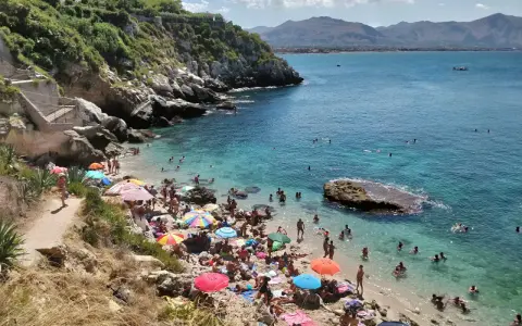 Affollata baia dei Francesi con gente che prende il sole e nuota nelle acque cristalline.