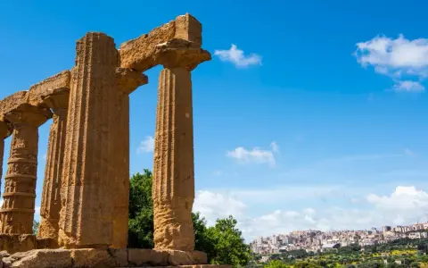 Colonne doriche imponenti, testimoni del **significato** di Akragas, con una città moderna sullo sfondo.