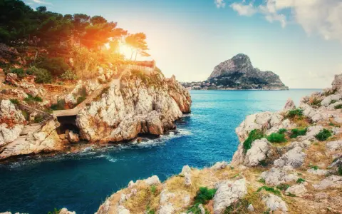 Scogliere rocciose e mare blu intenso vicino a Milazzo, con sentieri che scendono verso l'acqua. Le spiagge di Milazzo offrono panorami mozzafiato.