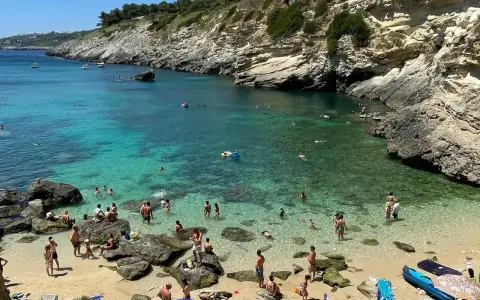 Spiaggia 100 gradini Mongerbino, con acque cristalline e scogliere rocciose. Persone nuotano e prendono il sole in una giornata estiva.
