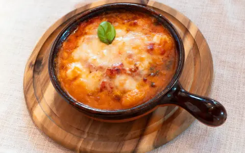 Piatto fumante di gnocchi al forno, uno dei piatti tipici della Campania, con pomodoro e mozzarella filante, guarnito con basilico.