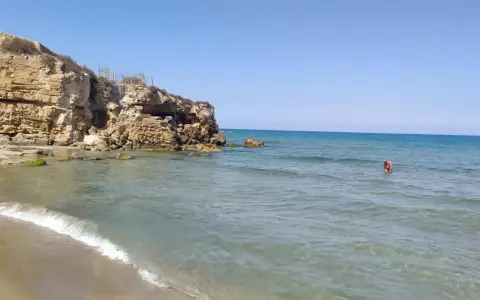 Spiaggia di Eloro con scogliere rocciose, mare azzurro e una persona che fa il bagno.