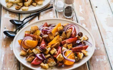 Un piatto di panzanella siciliana con pomodori, cipolla rossa e crostini croccanti.