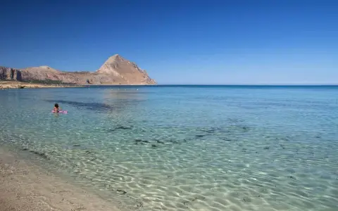 Bambina su un materassino rosa galleggia nelle acque cristalline della macari spiaggia, con montagne sullo sfondo.