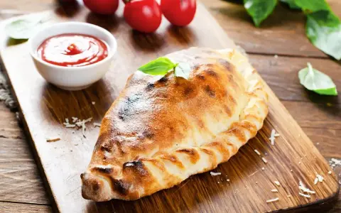 Un dorato cudduruni palermitano, guarnito con basilico, su tagliere di legno, con pomodorini e salsa di pomodoro.