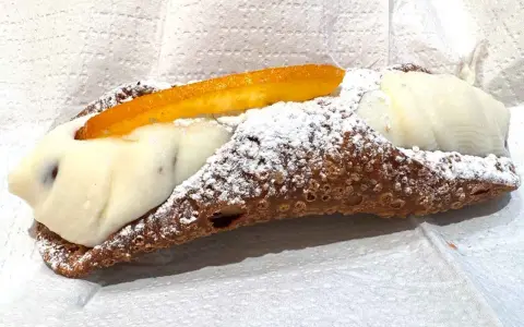 Cannolo ripieno di ricotta, uno dei dolci tipici di Palermo, cosparso di zucchero a velo e decorato con scorza d'arancia candita.