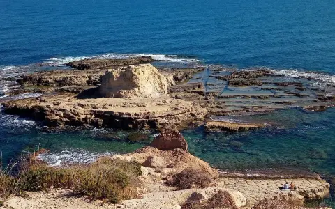 Scogliera rocciosa con acqua cristallina, dove si narra avvenne lo sbarco dei turchi. Due persone sedute ammirano il panorama.