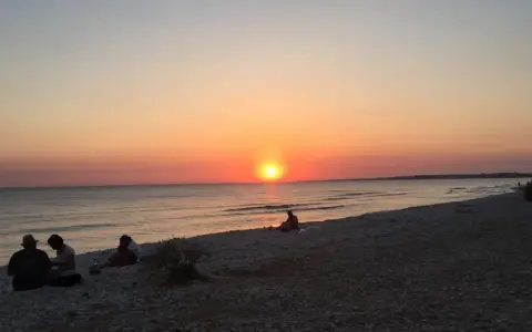 Tramonto sulle menfi spiagge più belle. Persone sedute sulla riva, godendosi la vista del sole che cala sul mare.