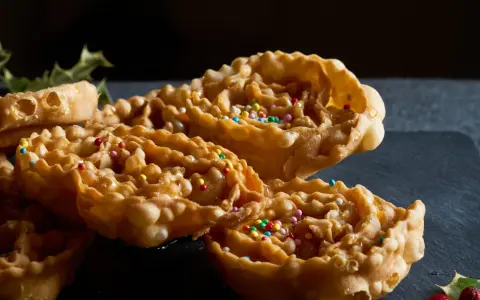 Cartellate, dolci tipici della Puglia, ricoperte di miele e confettini colorati, con un rametto di agrifoglio sullo sfondo.