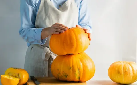 Mani che impilano zucche arancioni, una tagliata a metà su un tagliere. La cucuzza baffa è pronta per essere preparata.