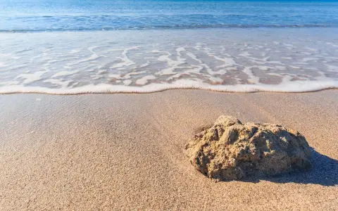 Onda che lambisce la sabbia dorata della spiaggia Tonnarella Mazara, con una roccia in primo piano.
